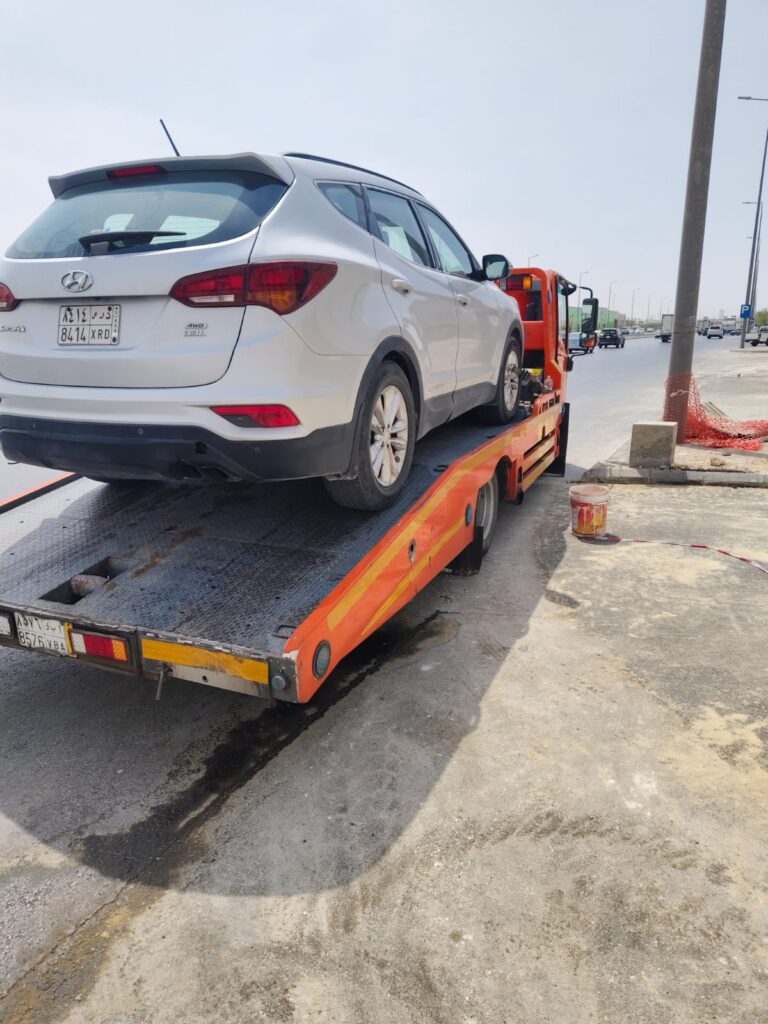 Silver Hyundai Santa Fe SUV loaded on an orange flatbed tow truck at the roadside