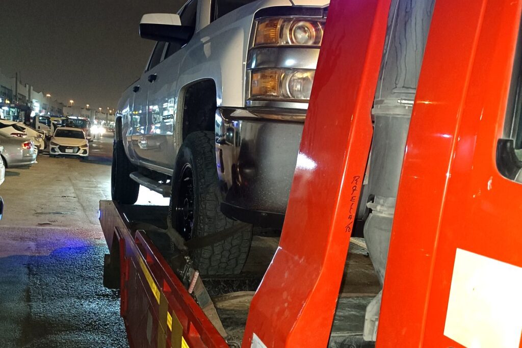 Satha Care flatbed tow truck carrying a pickup in Riyadh at night